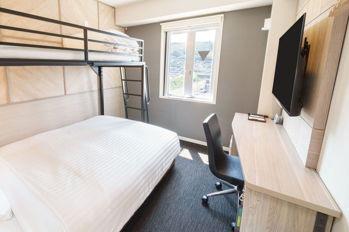 A bunk bed with a desk and chair, a TV, and a window with a view.