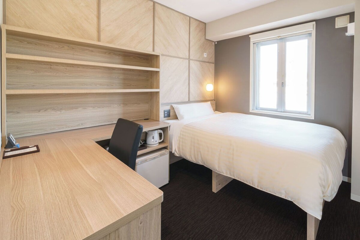 A bedroom with a bed, desk, chair, and a window.