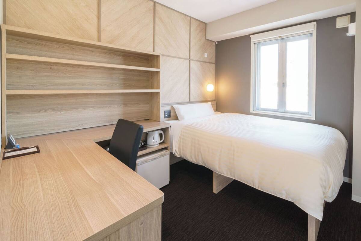 Un dormitorio con cama, escritorio, silla y ventana.