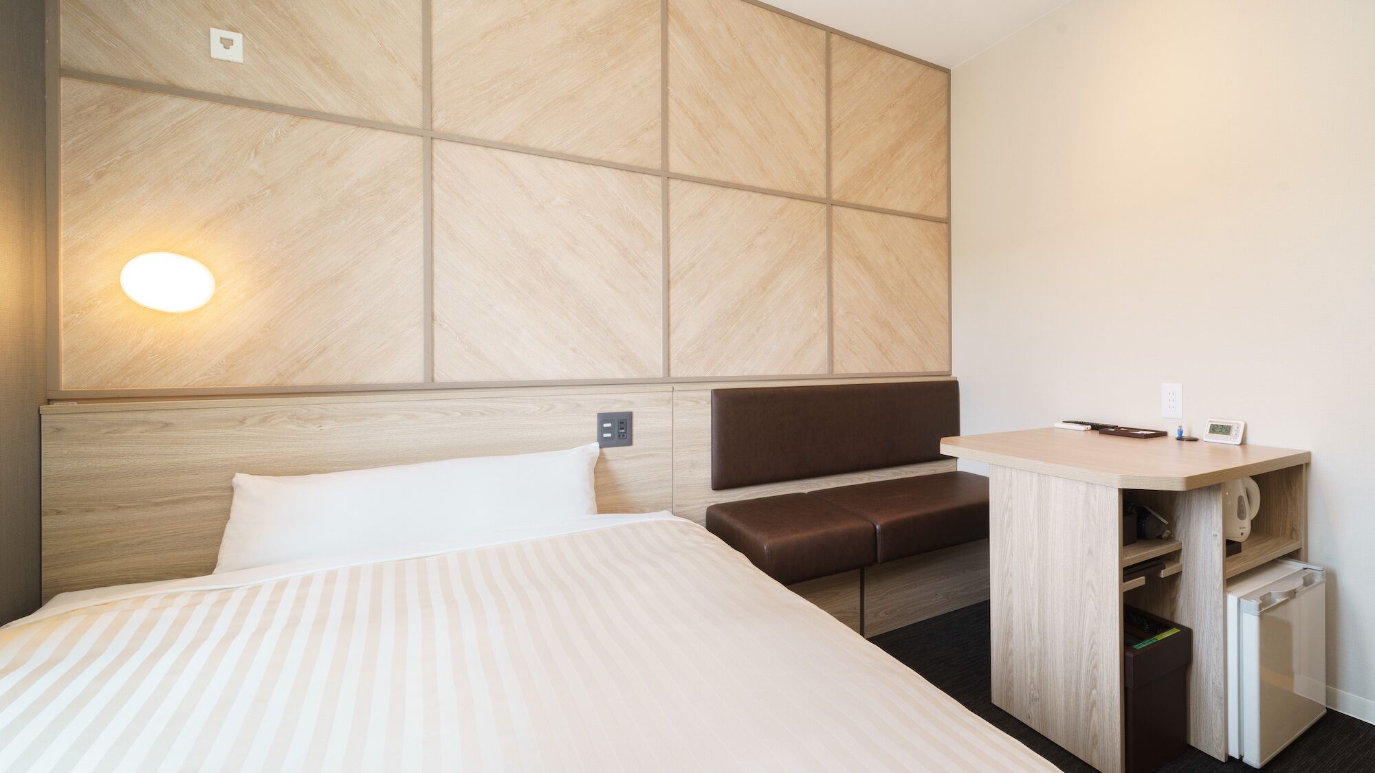 Une chambre d’hôtel comprenant un lit, un coin salon, un bureau avec une bouilloire et une lampe fixée au mur.