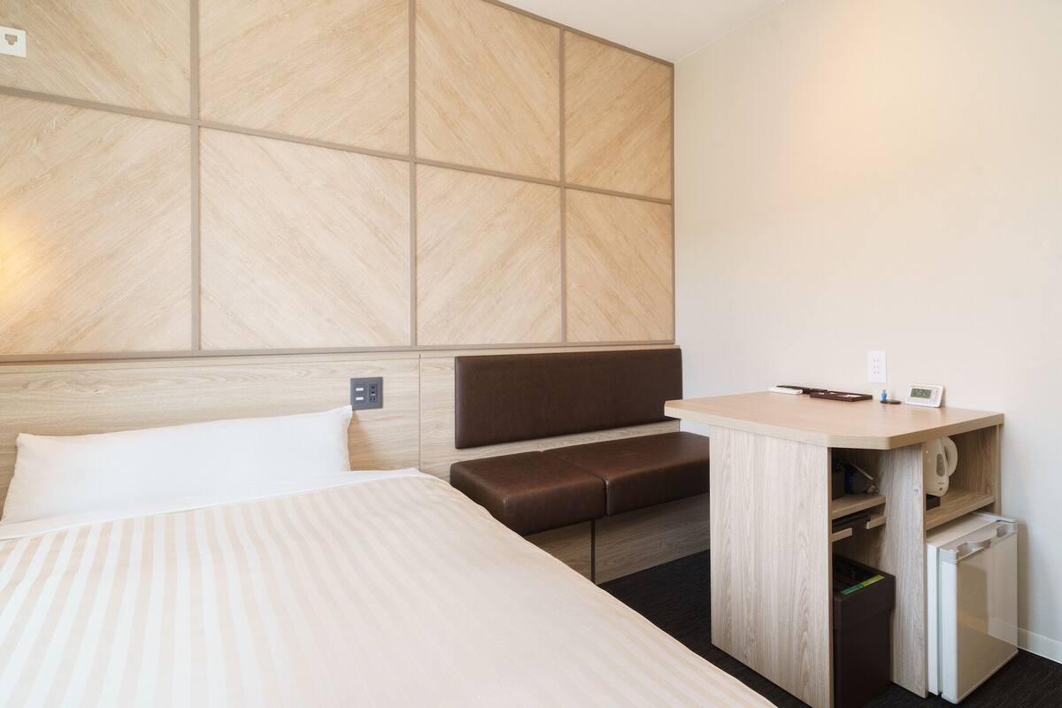 Habitación de hotel con cama, zona de estar, escritorio con hervidor y una lámpara de pared.