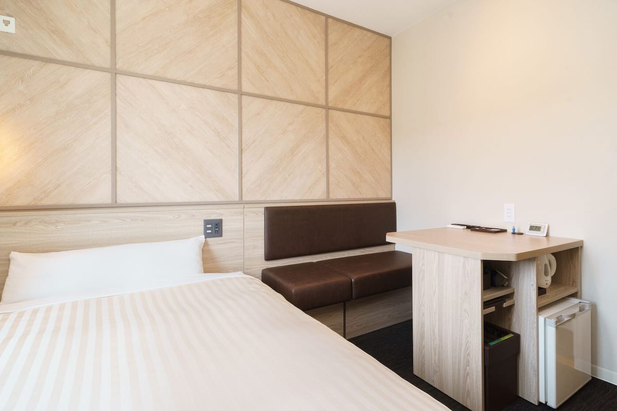 Une chambre d’hôtel comprenant un lit, un coin salon, un bureau avec une bouilloire et une lampe fixée au mur.