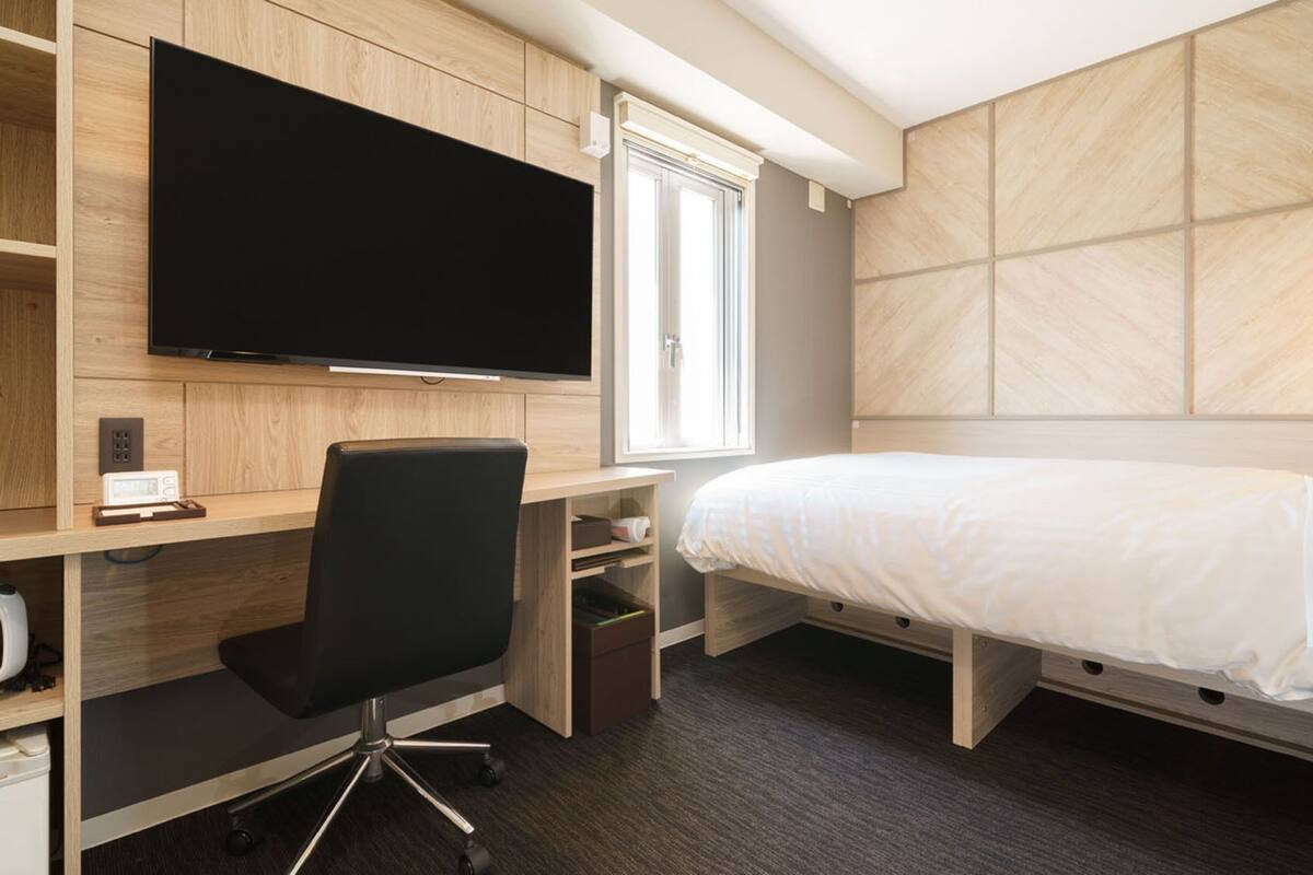 Una habitación de hotel compacta con cama, escritorio, silla, televisor y ventana.