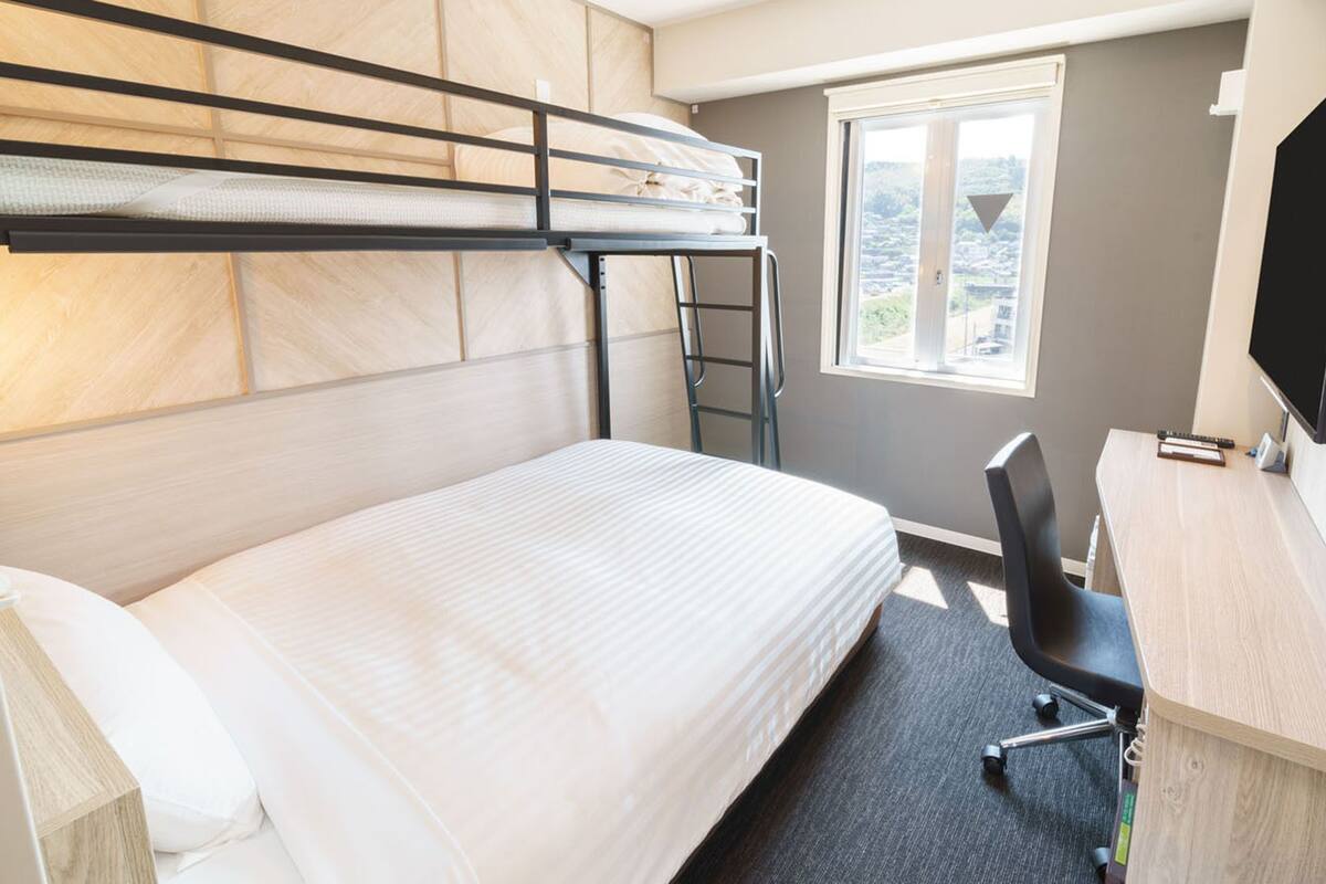 Una cama litera con escritorio y silla, un televisor y una ventana con vistas.