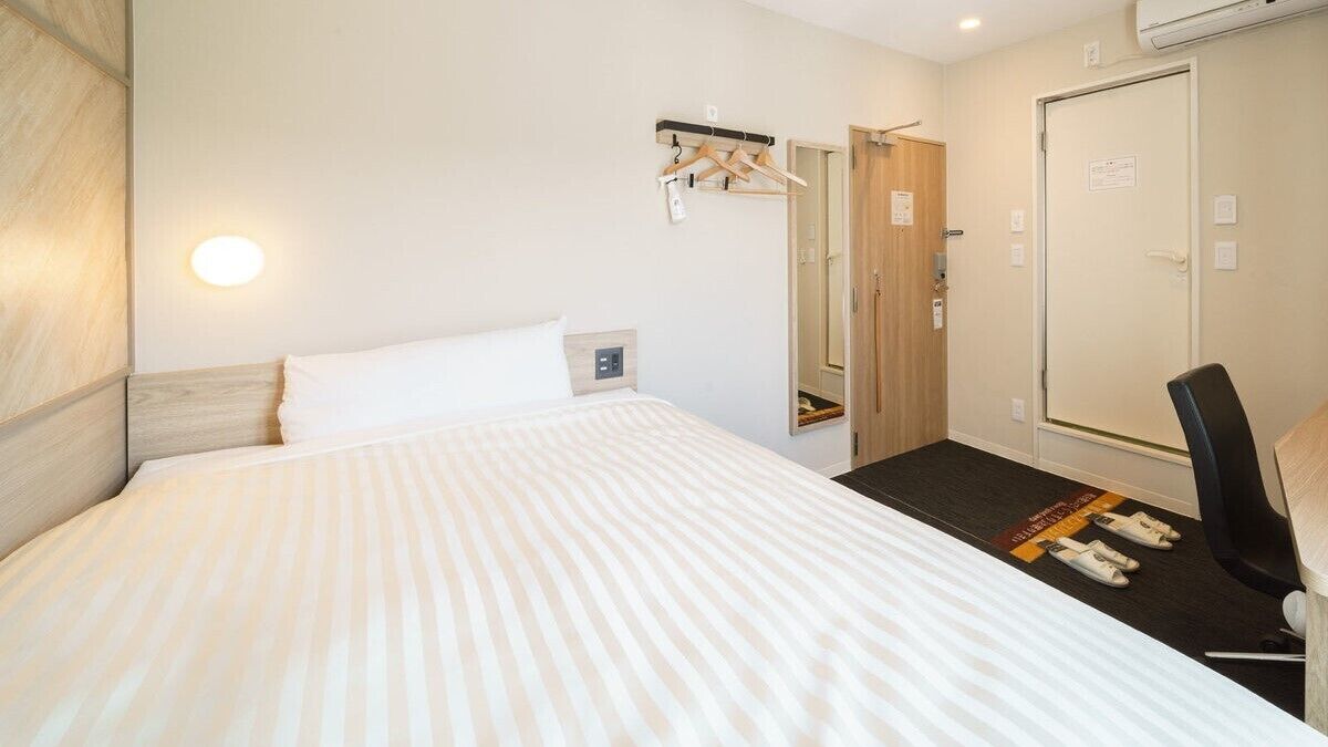 Une chambre d’hôtel comprenant un lit, une chaise, un porte-manteau, une armoire et un miroir.