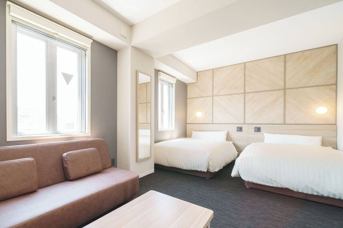 Habitación de hotel con sofá, dos camas, una mesita pequeña y ventanas amplias.
