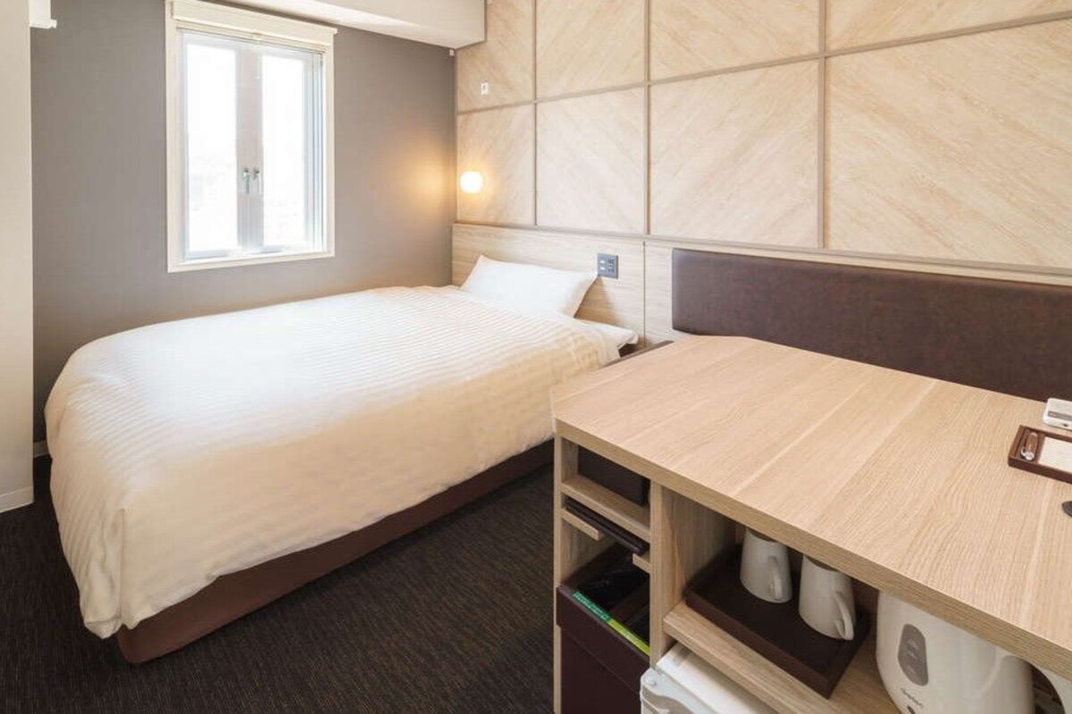 A compact hotel room with a single bed, a small desk, and a built-in wardrobe.