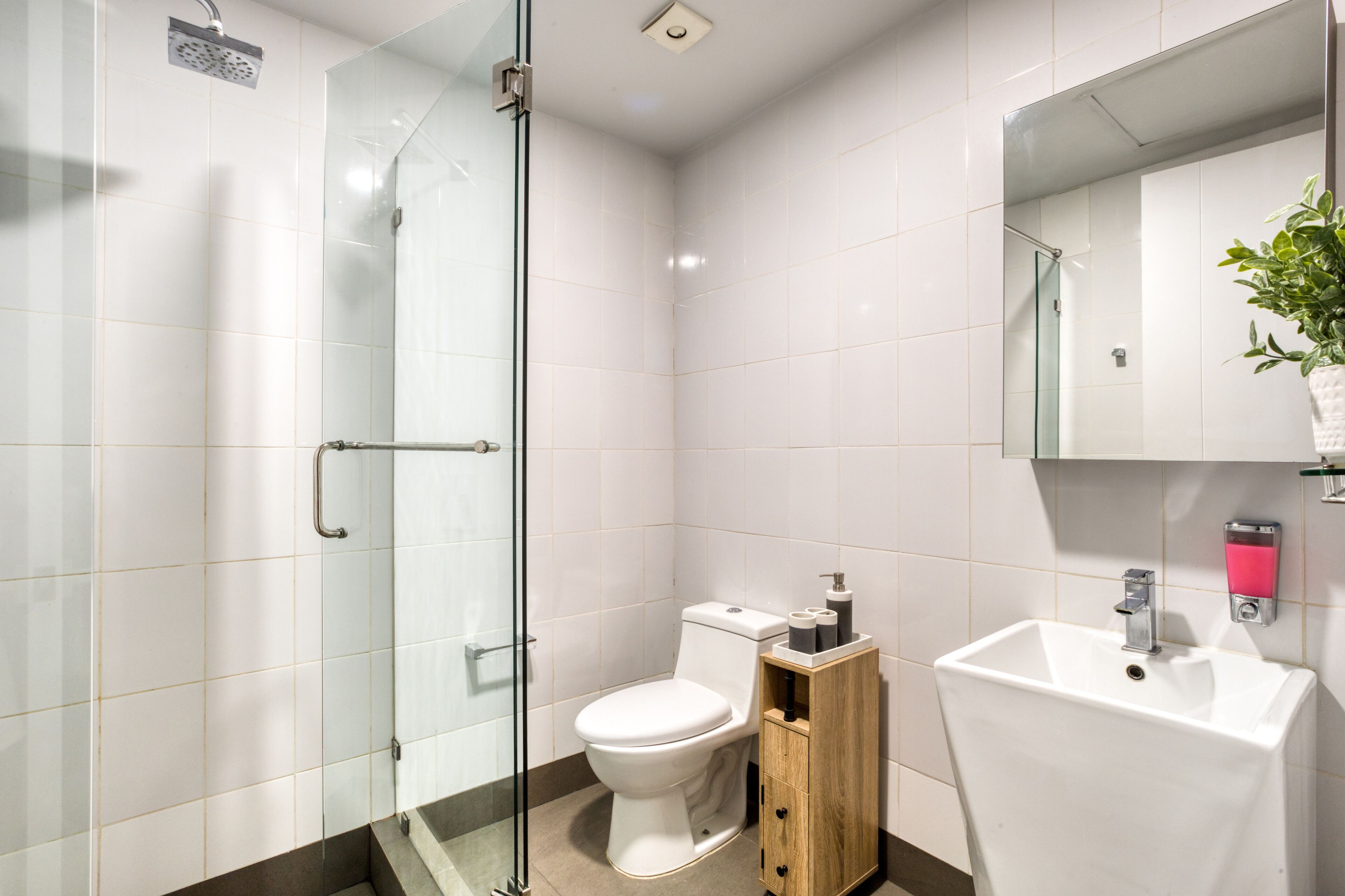 A modern bathroom with a glass shower enclosure, a white toilet, a wooden cabinet, and a white sink with a mirror above it.