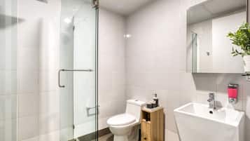 A modern bathroom with a glass shower enclosure, a white toilet, a wooden cabinet, and a white sink with a mirror above it.