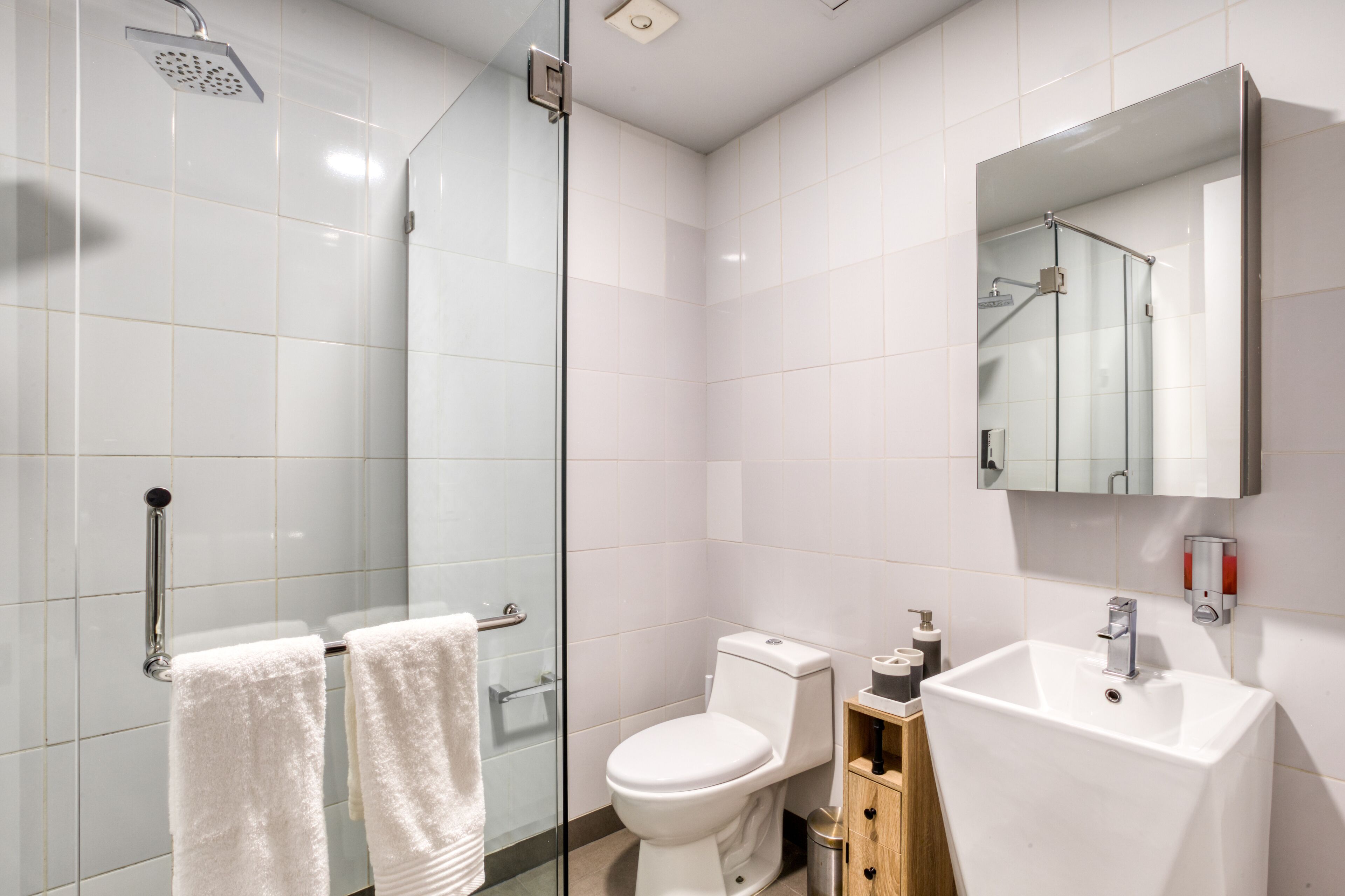 Een moderne badkamer met een douchecabine van glas, een wit toilet en een wastafel met spiegel erboven.