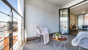 A balcony with a chair, a table with a plant and wine glass, and a view of a cityscape.
