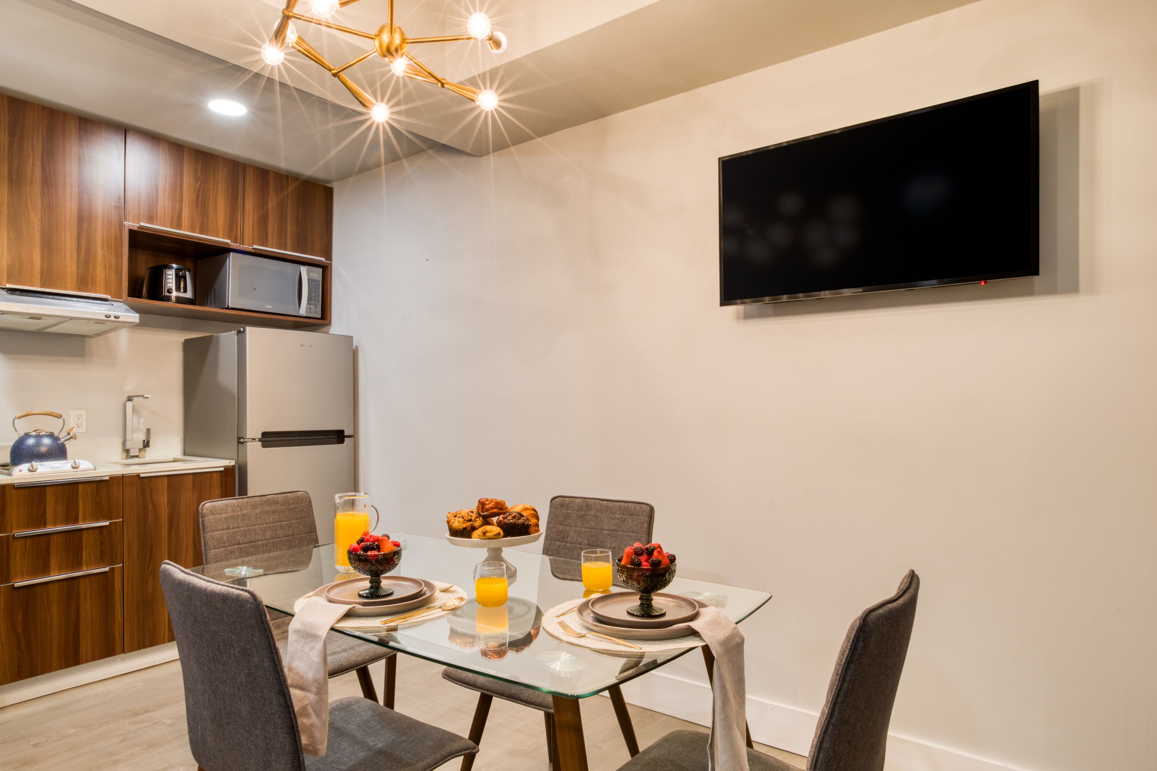 A modern kitchen with built-in appliances, a dining table with chairs, and a mounted TV.