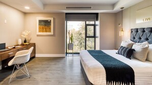 A modern bedroom with a bed, a desk, and a chair. There is a window with a view of trees.