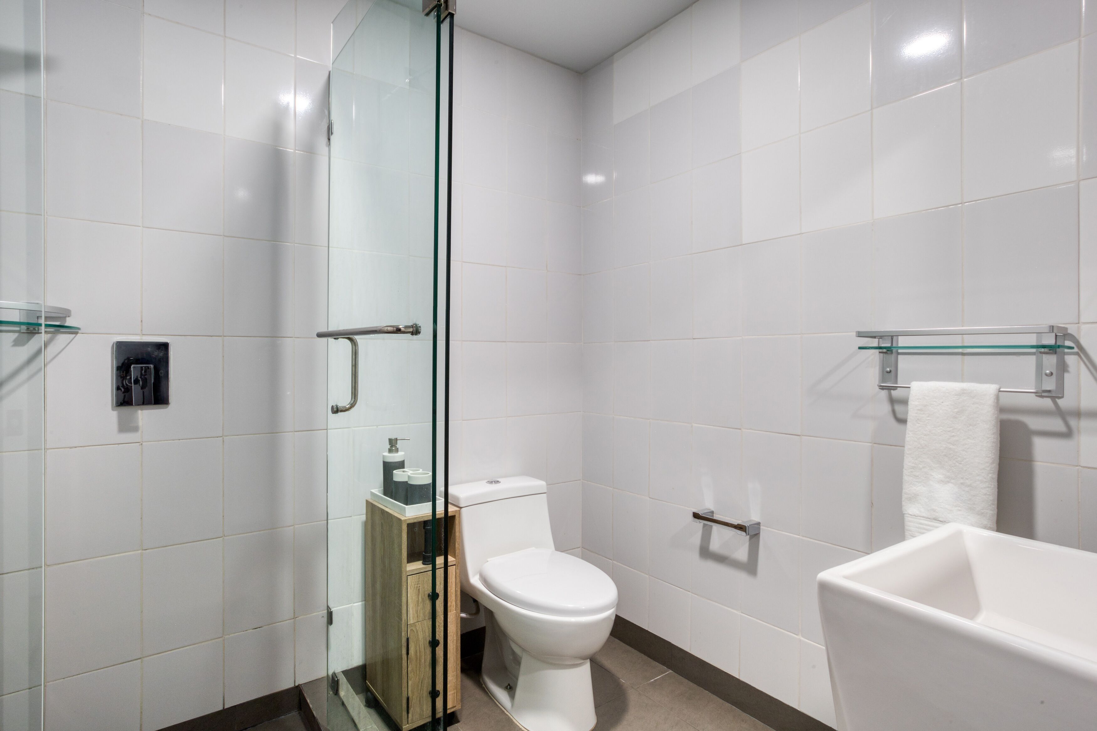 A modern bathroom with a glass shower enclosure, a white toilet, a bathtub, and a glass shelf with a towel.