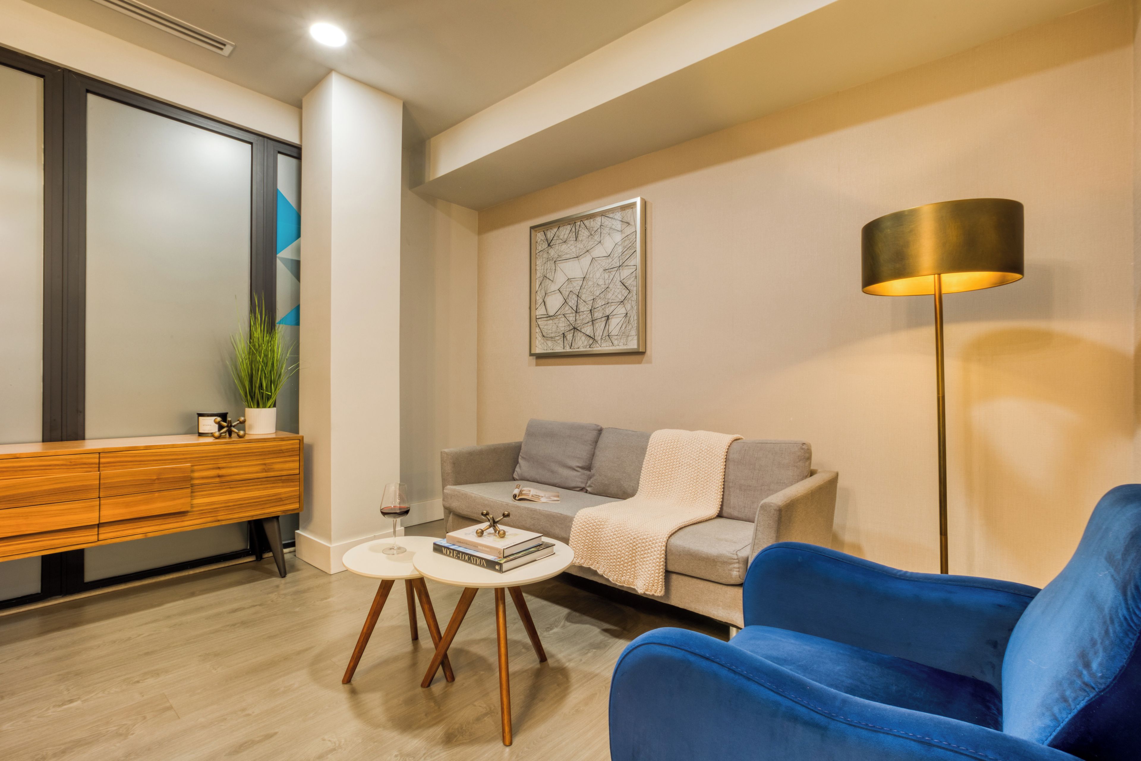 A modern living room with a sofa, a blue armchair, a coffee table, a floor lamp, and a painting on the wall.