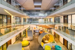 A modern hotel lobby with a glass atrium, seating areas, and a central staircase. - Eazy Rio by ULIV (Tijuana)