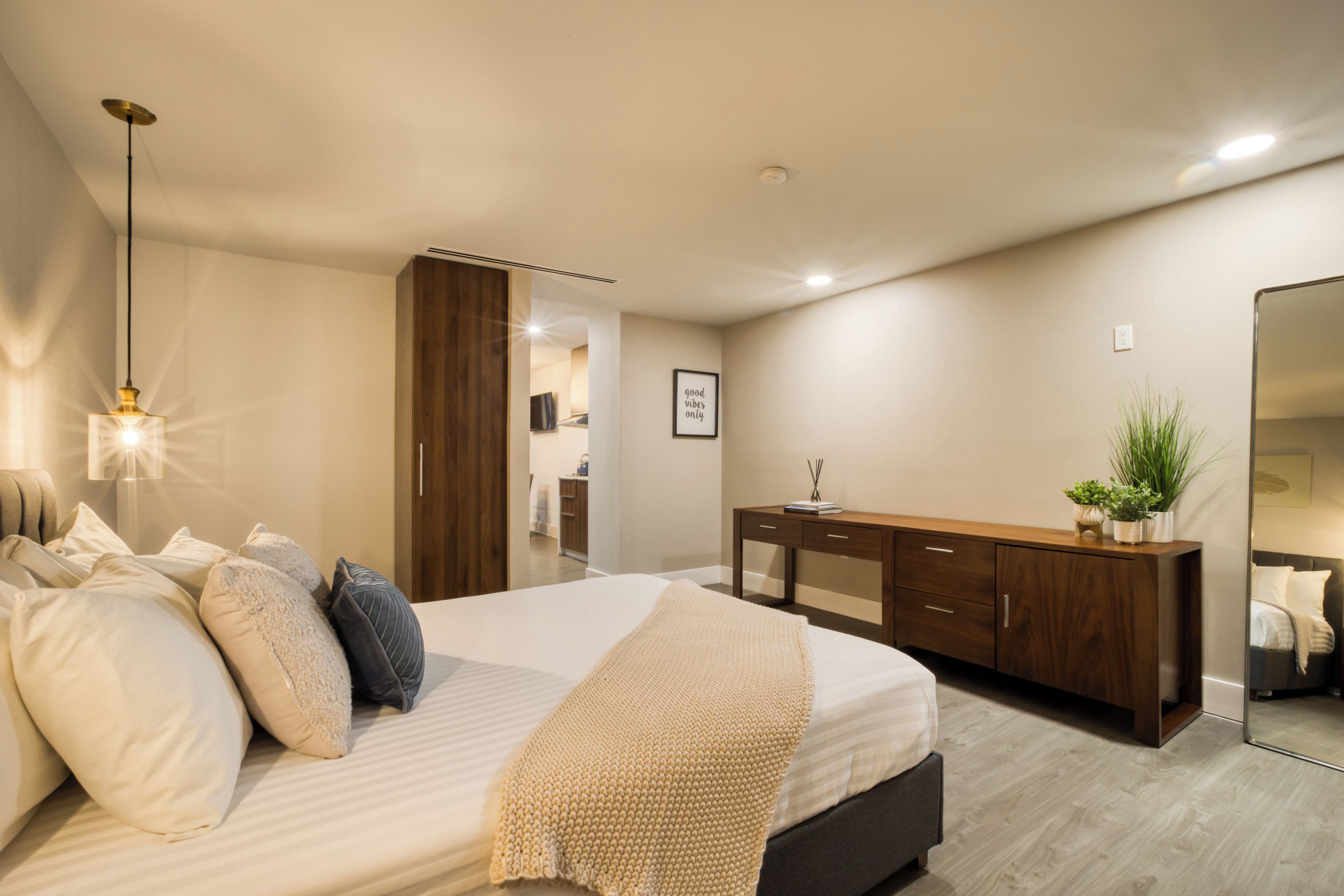 A modern bedroom with a large bed, bedside tables, a wooden dresser, and a mirror.