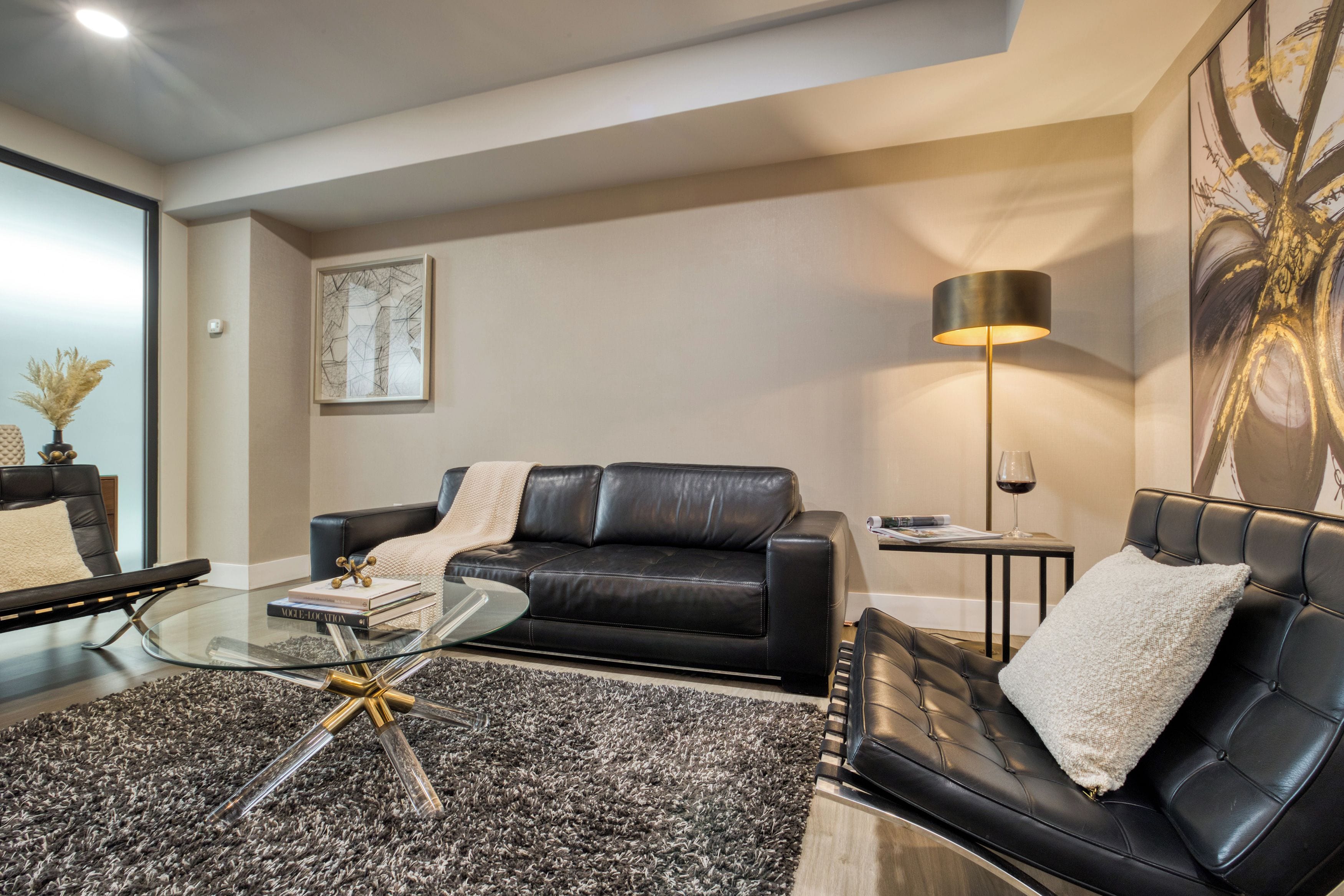 A modern living room with a black leather sofa, a glass coffee table, and a black floor lamp.