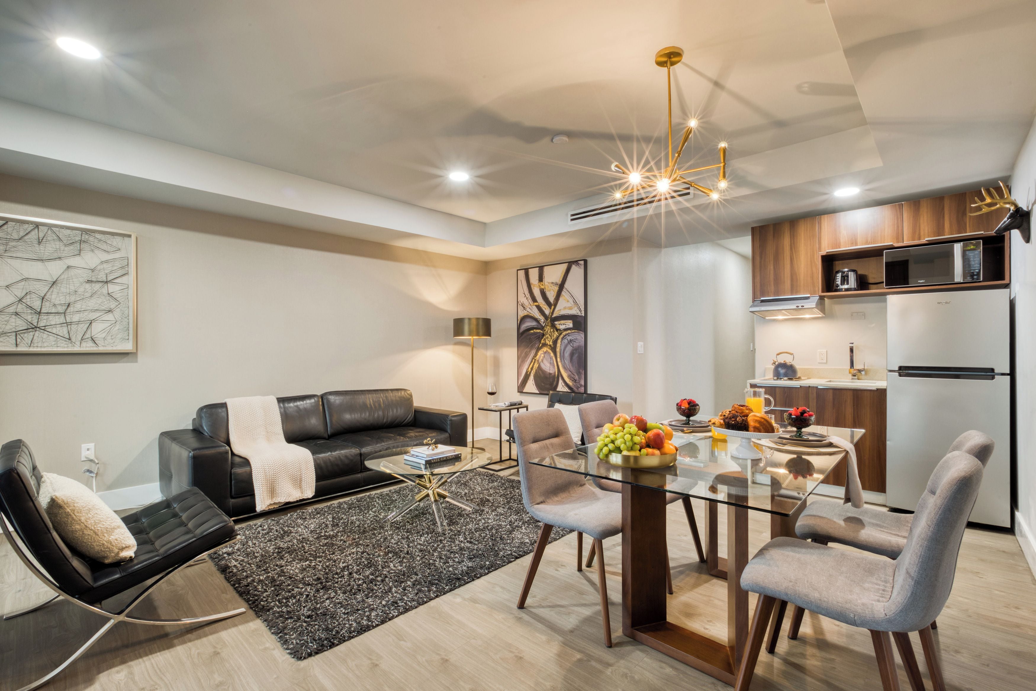 A modern living room with a black leather sofa, a glass coffee table, and a dining area with a glass table and chairs.