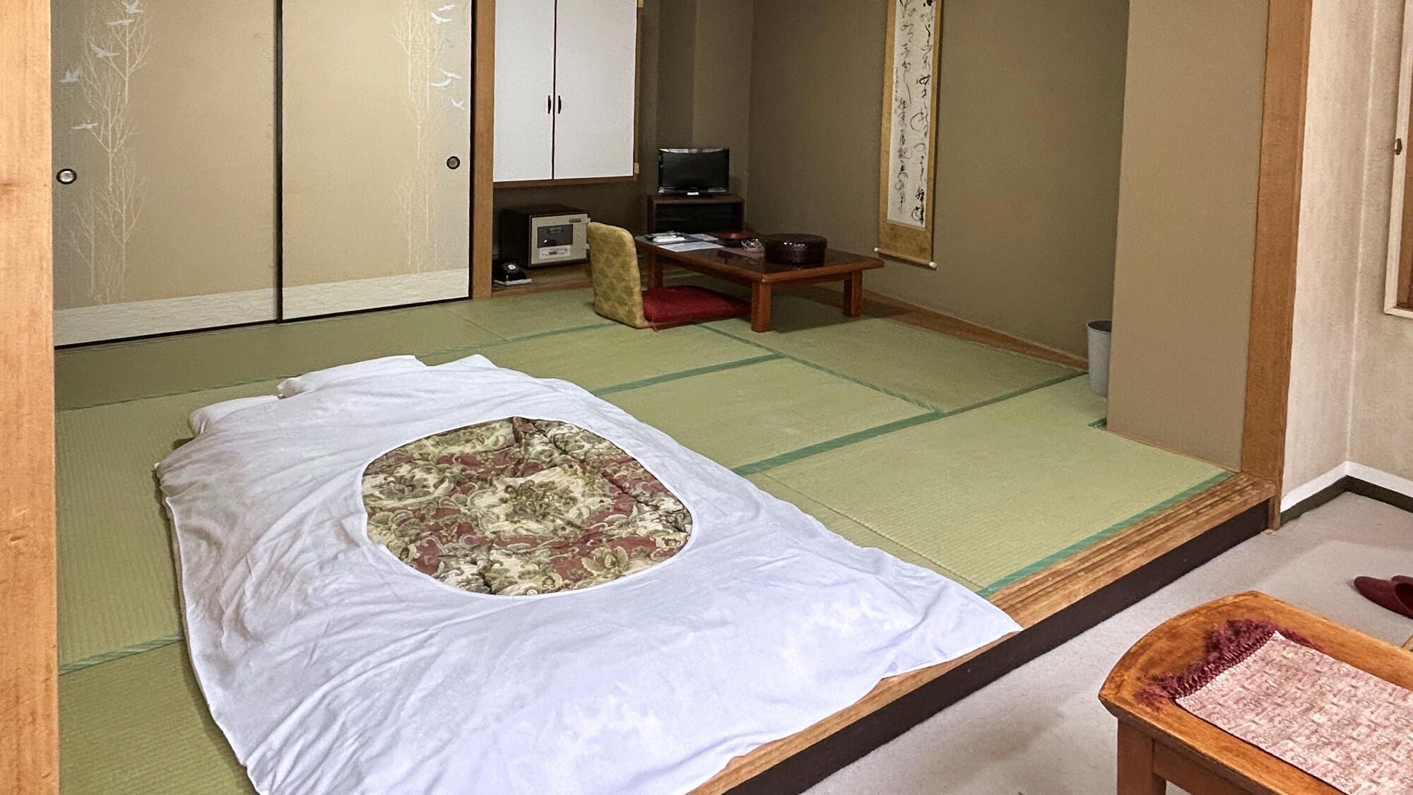 Une pièce de style japonais traditionnel, avec un sol recouvert de tatamis, un futon servant de lit, une télévision et un paravent en papier de riz (shoji).