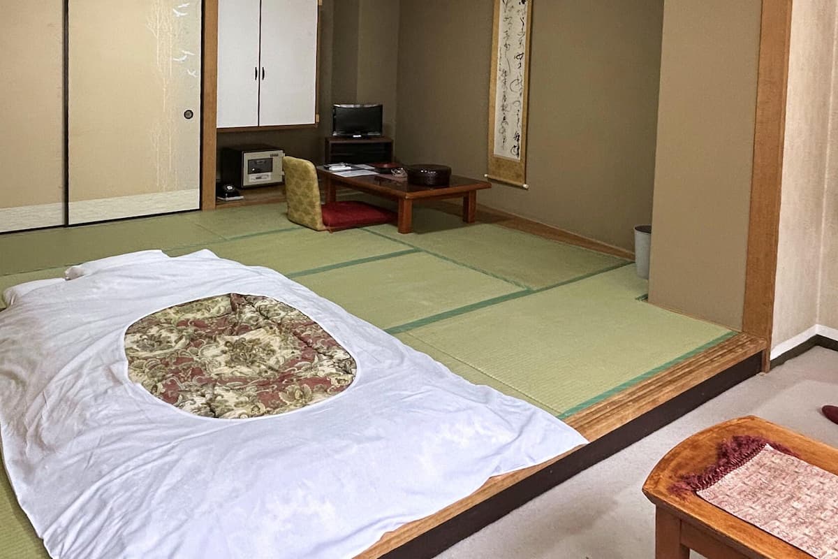 Une pièce de style japonais traditionnel, avec un sol recouvert de tatamis, un futon servant de lit, une télévision et un paravent en papier de riz (shoji).