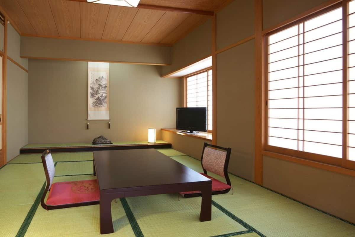 Une pièce de style japonais traditionnel, avec un sol recouvert de tatamis, une table basse, un téléviseur et des portes coulissantes.