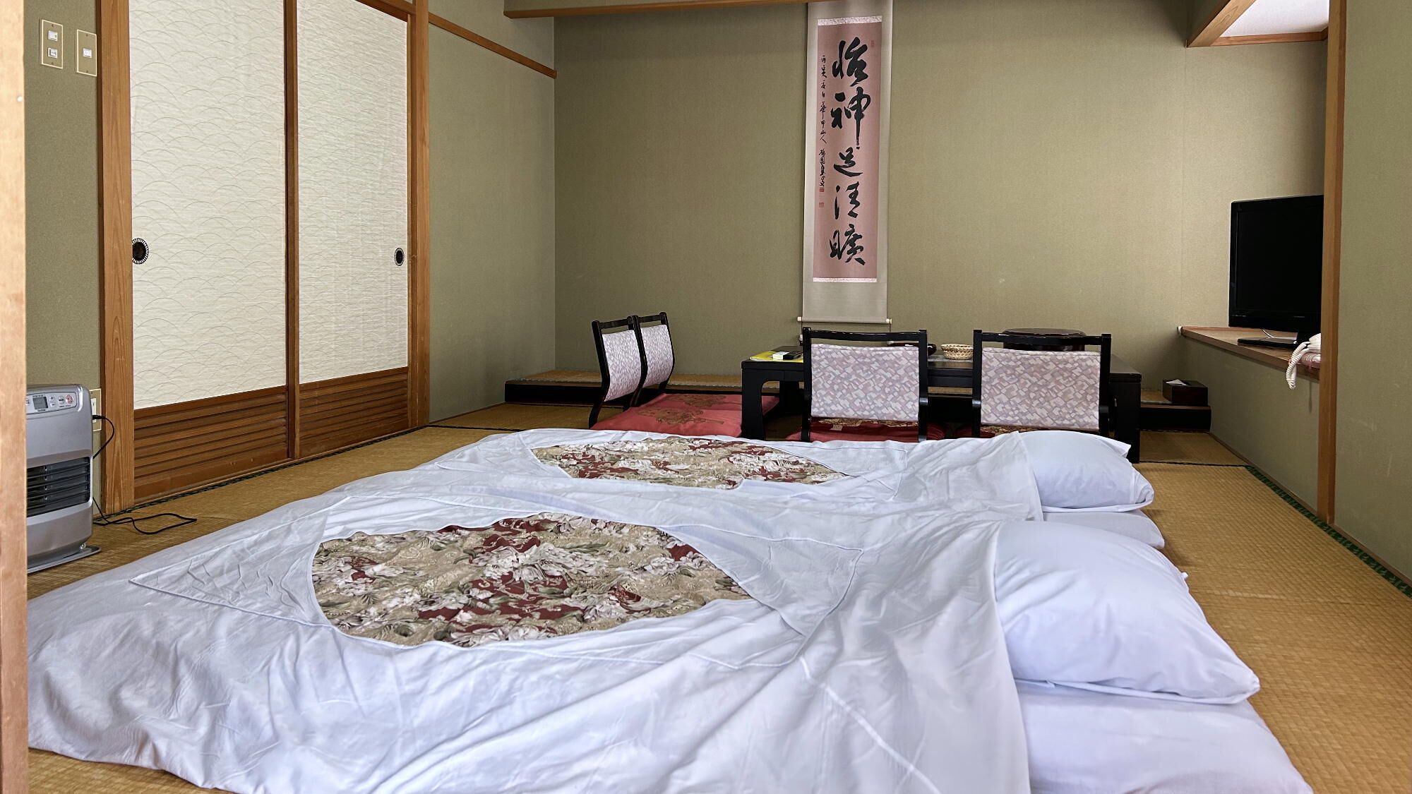 Une pièce de style japonais traditionnel, avec un sol recouvert de tatamis, un futon servant de lit, un paravent en papier de riz (shoji), un bureau avec un téléphone et un téléviseur.