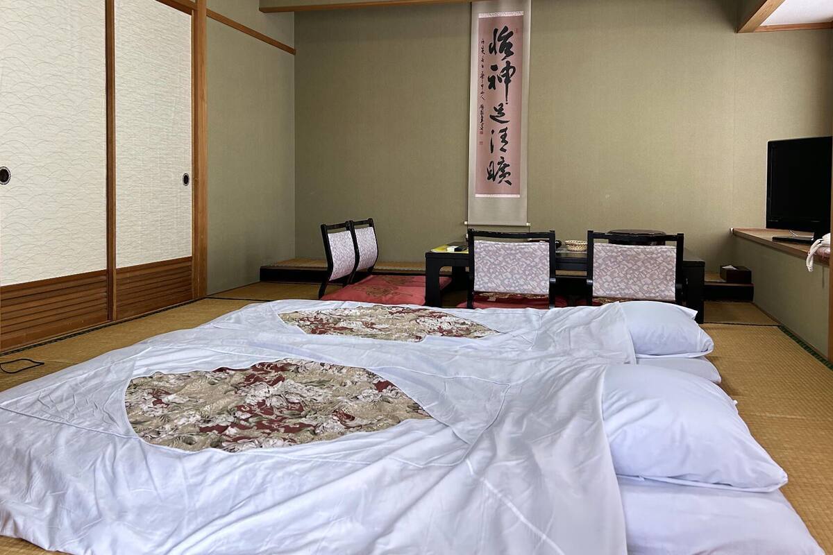 Une pièce de style japonais traditionnel, avec un sol recouvert de tatamis, un futon servant de lit, un paravent en papier de riz (shoji), un bureau avec un téléphone et un téléviseur.