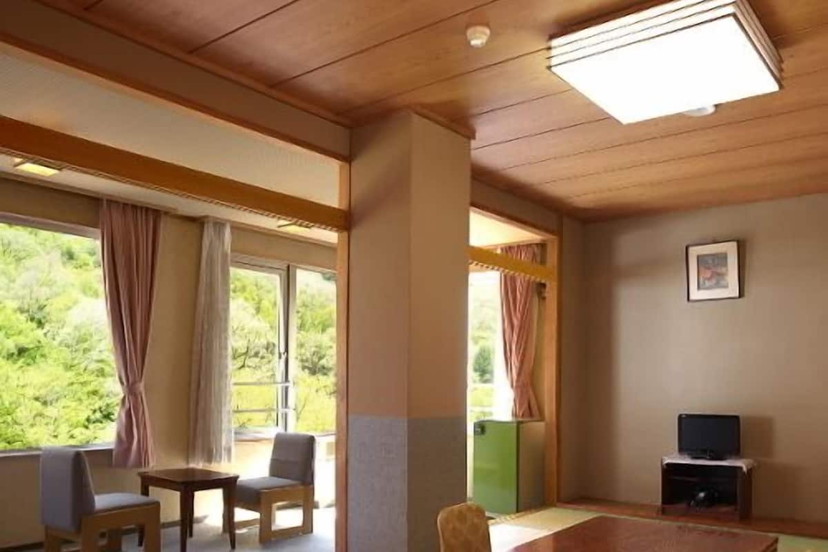 Une pièce avec des tatamis, une table en bois, des chaises, un téléviseur et une fenêtre avec des rideaux.