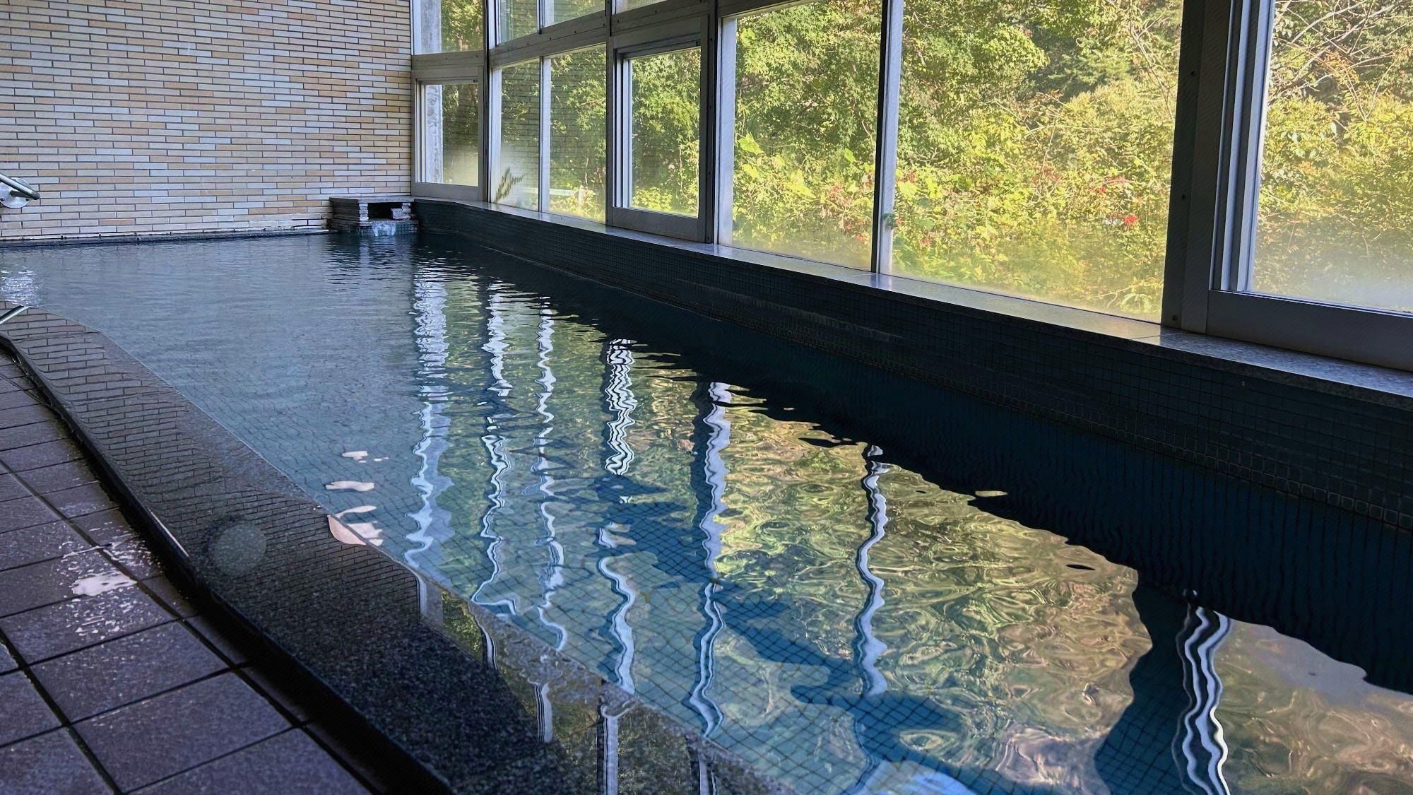 A swimming pool with clear water, surrounded by a tiled walkway and a brick wall.