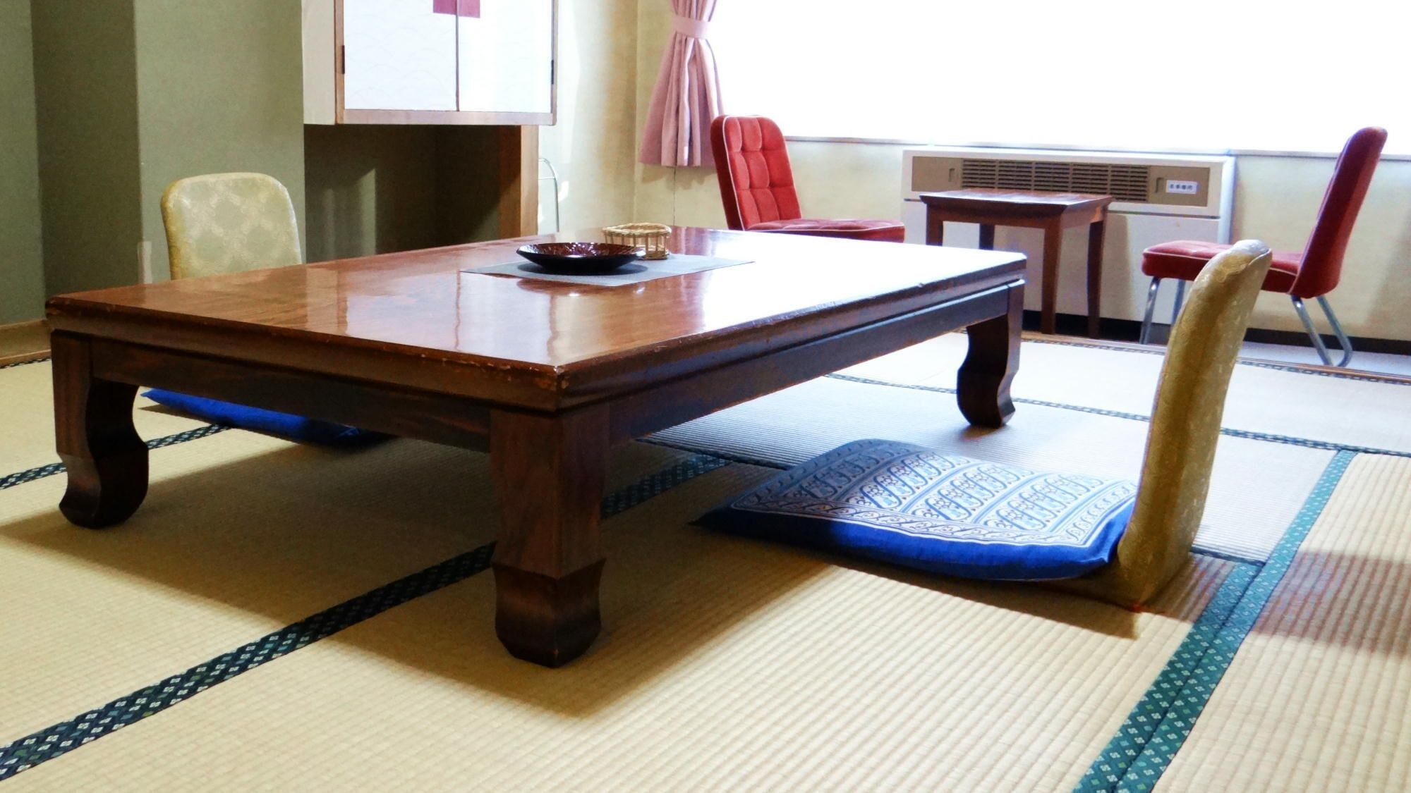 Une pièce de style japonais traditionnel, avec un sol recouvert de tatamis, une table en bois, des chaises et une petite table sur laquelle se trouve un bol.
