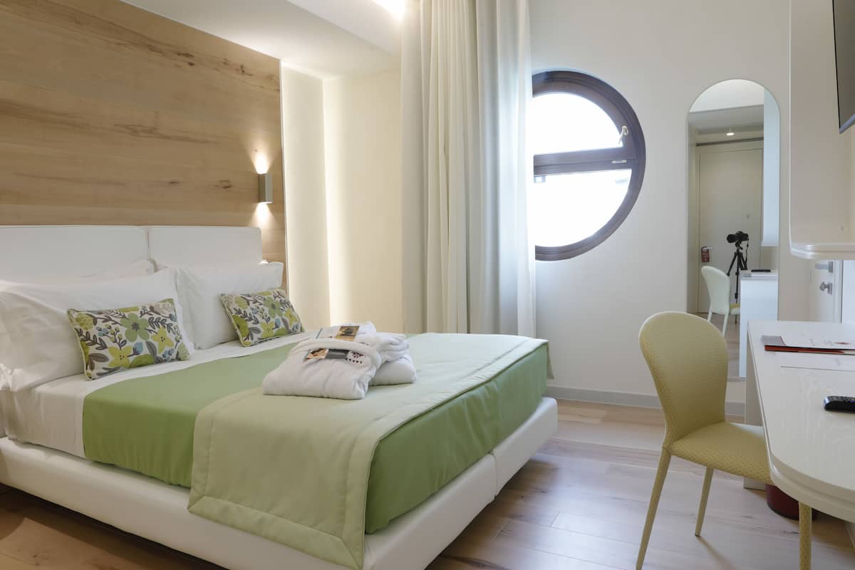 Una habitación de hotel con una cama, una silla, un escritorio y un ventanal redondo.
