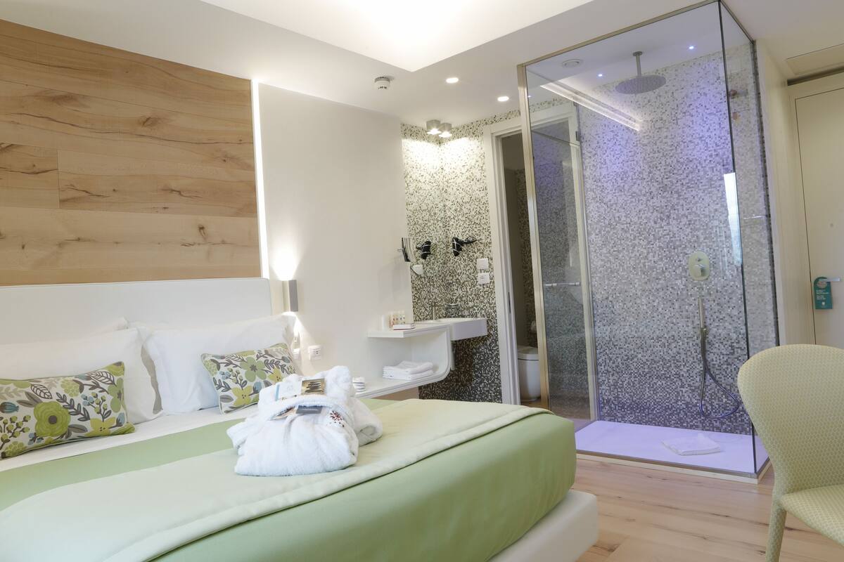Una habitación de hotel moderna con una cama grande, zona de ducha y espacio de descanso.