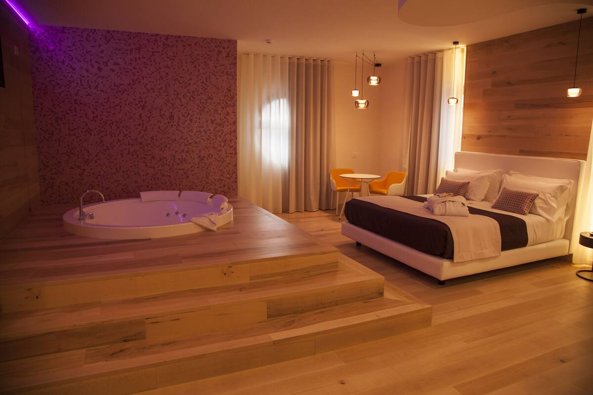Un dormitorio moderno con una cama grande, una mesita redonda y una bañera.
