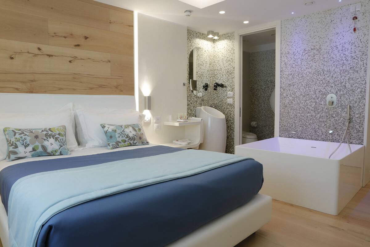 Un dormitorio moderno con una cama grande, una mesita de noche, una bañera integrada y una pared de madera.