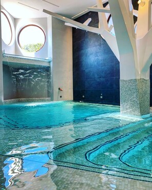 An indoor swimming pool with clear water, a tiled floor, and a modern architectural design. - Astrea Wellness & Spa (Altavilla Silentina)