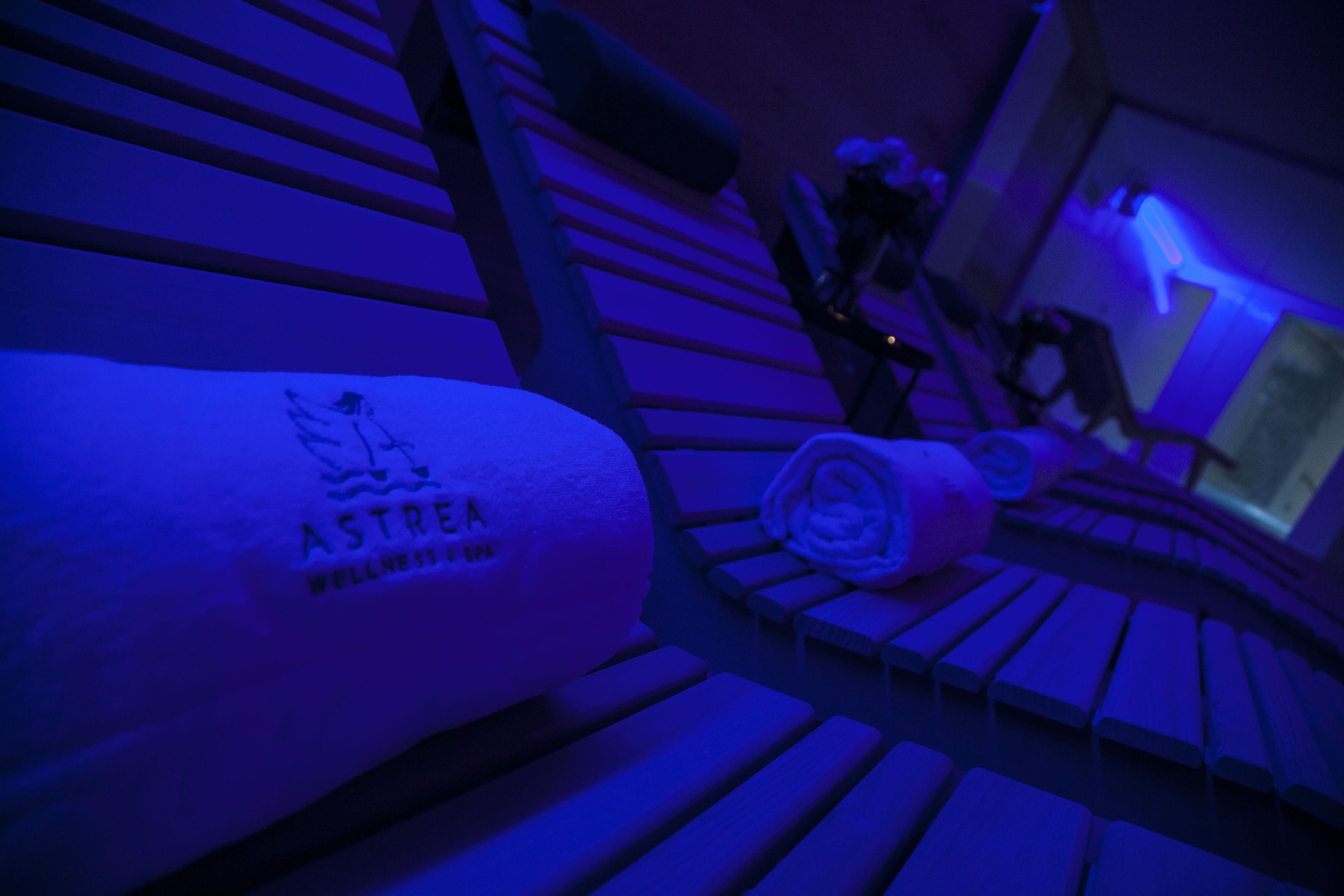 A room with a massage chair, a towel with 'ASTREA WELLNESS SPA' branding, and a window in the background.