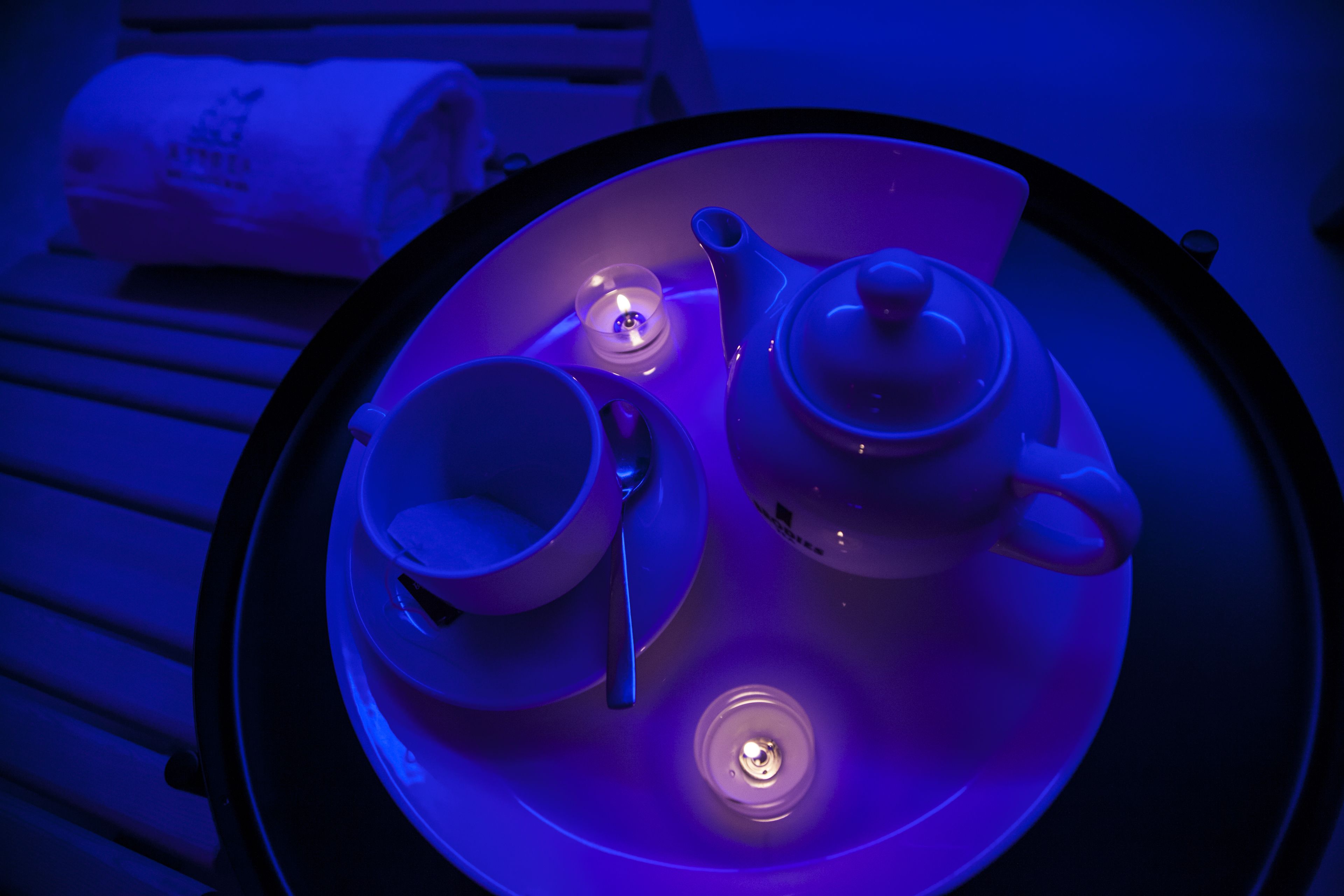 Une table avec une théière, une tasse et une soucoupe, ainsi qu’une bougie et une serviette enroulée.