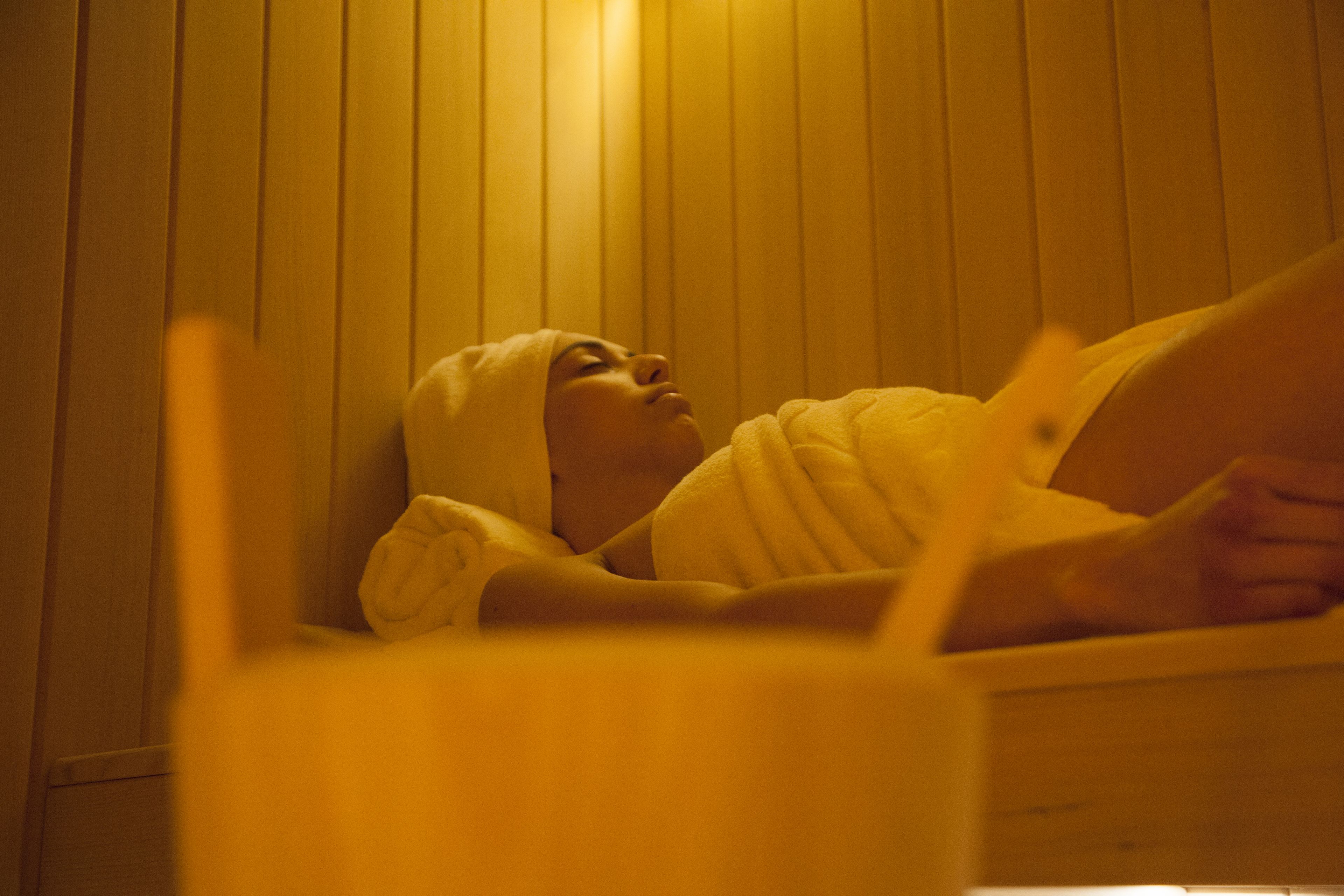 A person lying in a bathtub with wooden paneling on the walls.