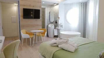 Habitación de hotel con cama, una mesa redonda, dos sillas, televisor, espejo y ventana con cortinas.