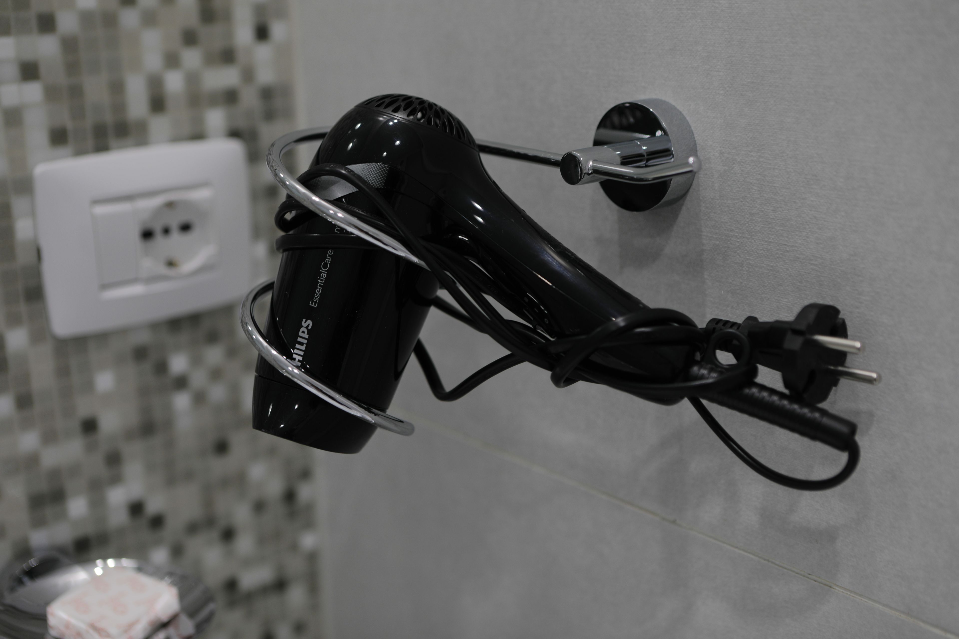 A hair dryer mounted on a wall with a power outlet nearby.