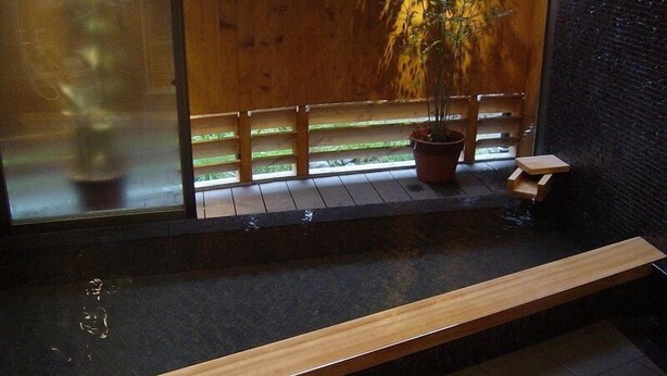 Eine Holzbank neben einem schwarz gefliesten Pool mit Holzzaun und einem Blumentopf.