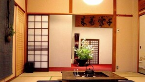 Ein traditioneller japanischer Raum mit Tatami-Böden, einem Shoji-Bildschirm, einem Tisch aus Tatami-Matten, einem Tee-Set und einer aufgehängten Schriftrolle.