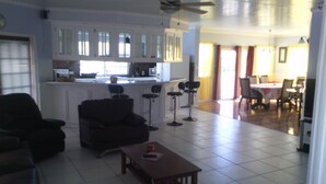A spacious living area with a dark-colored sofa, a wooden coffee table, and a kitchen area with white cabinets and a bar stool. - Rodney Heights Grande Splendour (Gros Islet)
