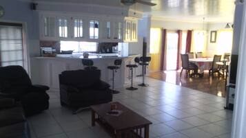 A spacious living area with a dark-colored sofa, a wooden coffee table, and a kitchen area with white cabinets and a bar stool.
