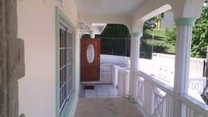 A covered porch with a wooden door and white railings. - Rodney Heights Grande Splendour (Gros Islet)