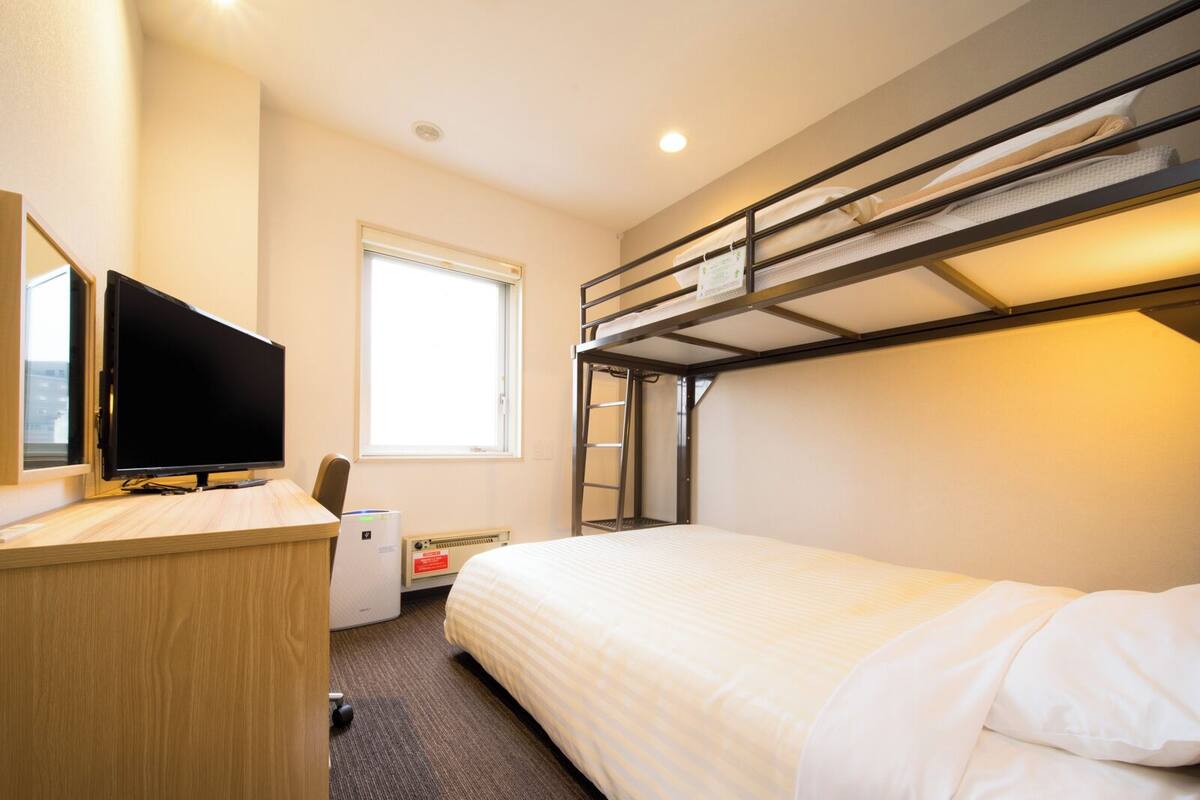Habitación de hotel con literas, un escritorio, un televisor de pantalla plana, una ventana y un radiador.