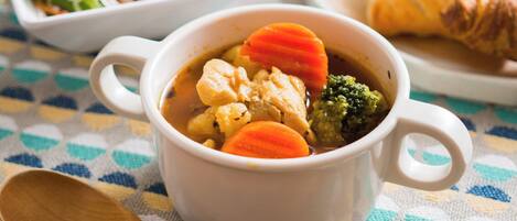 A meal with soup, including chicken, carrots, and broccoli, served in a white bowl with handles.