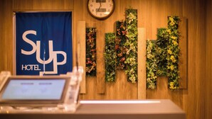 A hotel reception desk with a digital display, a clock, and vertical floral arrangements on the wall. - Super Hotel Kitami (Kitami)