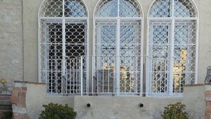 Ein Gebäude mit drei Rundbogenfenstern, Metallgitter, einer kleinen Treppe und verschiedenen Blumentöpfen.